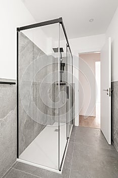 Bathroom with gray granite walls. The shower cabin is enclosed by glass transparent sliding doors in a black metal frame