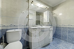 Bathroom of a home with two-tone tiles divided by a marine border, frameless mirror on the wall and white porcelain sink and