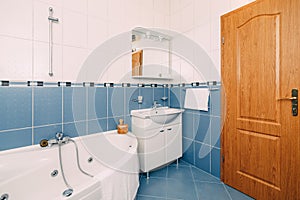 Bathroom with hydromassage bathtub, washbasin with mirror and brown wooden door.