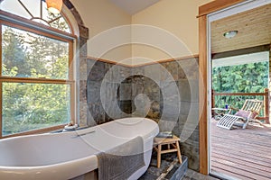 Bathroom interior with grey tiles and free standing white tub with open door to the balcony and oval window