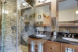 Bathroom interior with grey tiles and wak in shower with dark wood classic vanity with black countertop and two mirrors