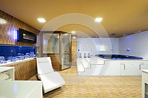 Bathroom with Jacuzzi, white sink, mirrors and Finnish sauna cabin with glass door