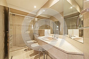 Bathroom with marble countertops, many mirrors, walk-in shower with hinged glass doors, and light brown toilets