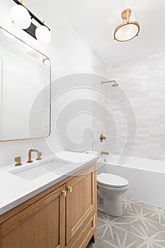 A bathroom with an oak cabinet and gold faucets and light fixtures.