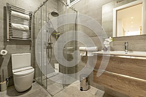 Bathroom with oak wood chest of drawers with imitation marble tiles, frameless mirror on the wall and glass shower cabin