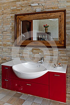 Bathroom red washbasin with mirror and a stone`s wall