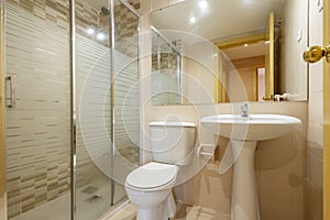 Bathroom with shower cabin with glass partition with chrome edges and frameless mirror covering the wall