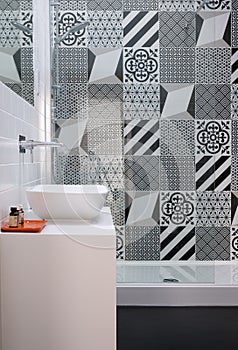 Bathroom with shower unit, toilet, bidet and basin unit, with black and white monochrome patchwork tiles and high ceiling