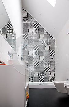 Bathroom with shower unit, toilet, bidet and basin unit, with black and white monochrome patchwork tiles and high ceiling