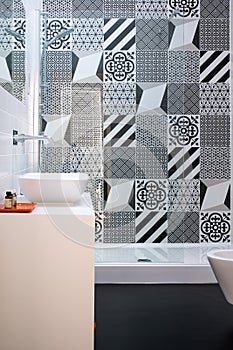 Bathroom with shower unit, toilet, bidet and basin unit, with black and white monochrome patchwork tiles and high ceiling