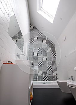 Bathroom with shower unit, toilet, bidet and basin unit, with black and white monochrome patchwork tiles and high ceiling