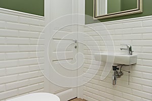 Bathroom, toilet room interior close-up. The walls are painted green, covered with decorative ceramic tiles with white glossy bric