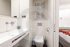 Bathroom with unusually designed sink, chrome taps and heated towel rail, frameless mirror and exit to a bedroom