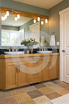 Bathroom vanity with wood cabinets, double sinks, slate tile floors and accent lighting in contemporary upscale home interior