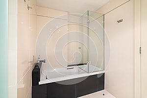 Bathroom with a white bathtub for bathing and relaxation in glossy black marble tiles. Faucet is built into a ledge