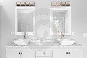 A bathroom with a white cabinet, vessel sinks, and bronze lights above the mirrors.