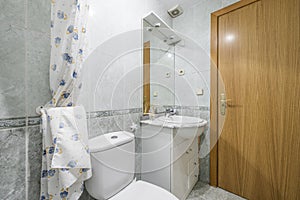 Bathroom with white furniture, mirror with sconces, oak wood door and two-tone tiles with a border