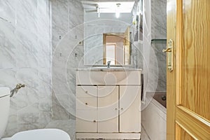 Bathroom with white porcelain shell sink with chrome faucet on water damaged wooden cabinet