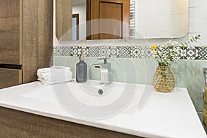Bathroom with a white porcelain sink with a wooden cabinet, a frameless mirror and a valance on the wall