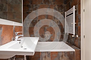 Bathroom with white porcelain wall-hung sink without cabinet, white wood-framed mirror, speckled tiles and white towel rail