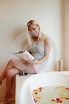 Bathtime with my favourite mag. A beautiful young woman reading a magazine while she sits on the edge of a luxurious