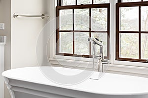 A bathtub faucet detail in front of a bright window.