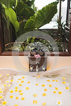 Bathtub with foam bubbles and yellow flowers with tropical garden view outside