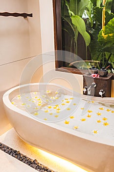 Bathtub with foam bubbles and yellow flowers with tropical garden view outside