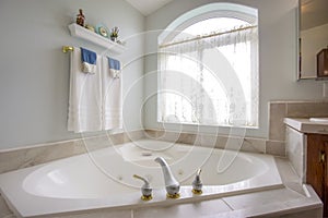 Bathtub with with gold and silver faucet beside an arched window with curtain