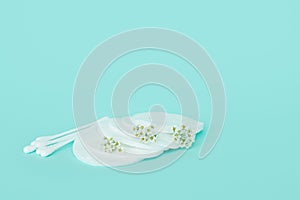 Batons and cotton buds for ears and makeup remover made of cotton on a turquoise background with small white flowers