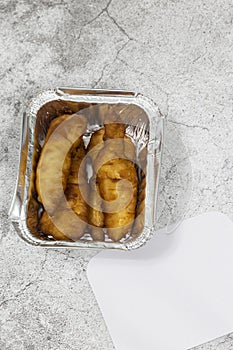 Battered chicken portions in a foil takeaway tray with lid.