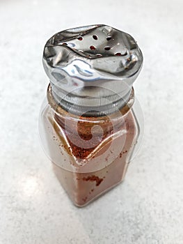 Battered old pepper shaker with ground red pepper on a lightly mottled stone background