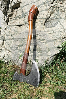 The battle ax is on the ground next to a large stone