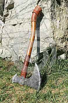 The battle ax is on the ground next to a large stone.