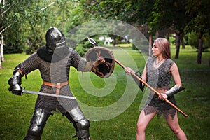 Battle of a fantasy warrior girl and a medieval knight in full set armor in the park