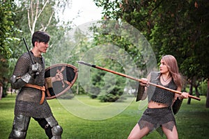 Battle of a fantasy warrior girl and a medieval knight in full set armor in the park