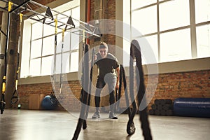 Battle ropes exercises. Young and strong man doing CrossFit exercises with a rope at gym