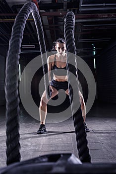 Battle ropes session. Attractive young fit and toned sportswoman working out in fitness training gym