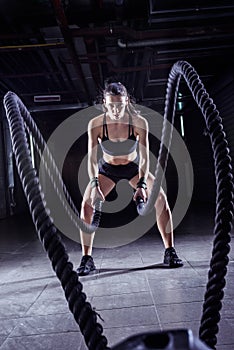 Battle ropes session. Attractive young fit and toned sportswoman working out in fitness training gym