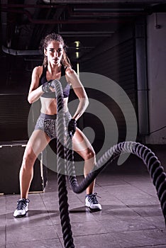 Battle ropes session. Attractive young fit and toned sportswoman working out in fitness training gym