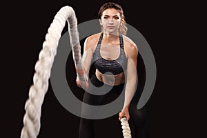 Battle ropes session. Attractive young fit and toned sportswoman working out in functional training gym doing crossfit
