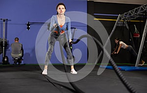 Battle ropes session. Attractive young fit and toned sportswoman working out in functional training gym doing crossfit