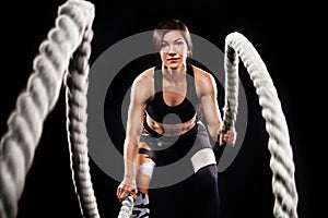 Battle ropes session. Attractive young fit and toned sportswoman working out in functional training gym doing crossfit