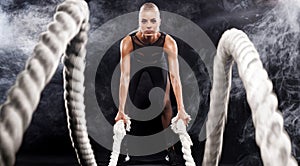 Battle ropes session. Attractive young fit and toned sportswoman working out in functional training gym doing exercise