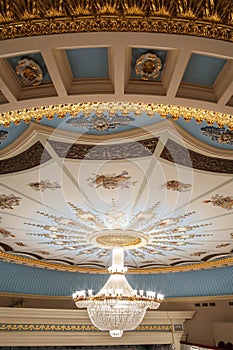 Large chandelier hangs on the theater hall decorated ceiling