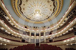 The interior of the hall in the theater with large chandelier hangs on the decorated ceiling