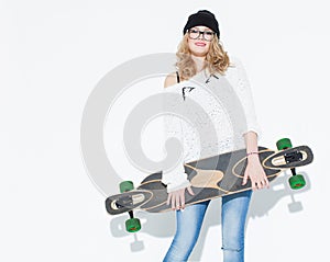 Bautiful fashionable cheerful young girl in a white sweater and longboard posing near white wall. In the studio photo