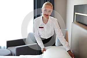 Bautiful maid setting up white pillow on bed sheet in hotel room