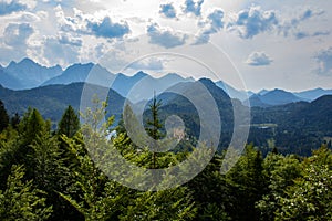 The Bavarian landscape with high forest covered mountains and castles are visible under a cloudy summer sky in Hohenschwangau,