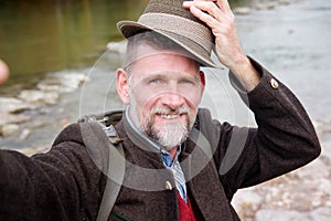 Bavarian man in his 50s standing by river and taking a selfie